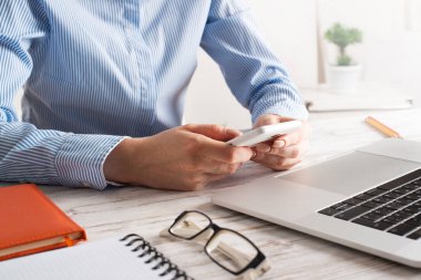 İş kadını cep telefonuyla masada oturuyor.