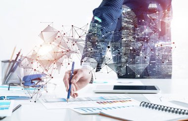 İş kadını elinde kalemle ofis masasının yanında duruyor.