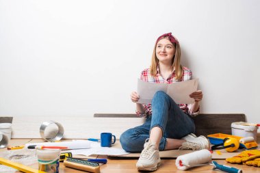 Mutlu güzel kız elinde planla yerde oturuyor.