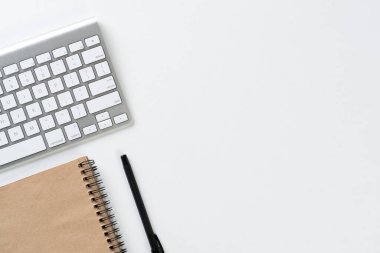 Modern iş yerinin en iyi manzarası. Beyaz yüzeyde spiral defter, kalem ve bilgisayar klavyesi. Eğitim, yaratıcılık ve fotokopi alanı ile yenilik kavramı. Modern ticarette dijital teknoloji.