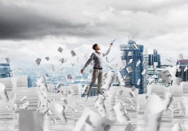 Sıradan giyinen bir adam kitapla el ele tutuşurken arka planda şehir manzarası olan uçan kağıt belgelerin arasında dikiliyor. Karışık ortam.