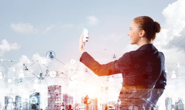 İş kadını akıllı telefonuyla selfie çekiyor. Şehir merkezindeki mimari ve takım elbiseli güzel bir kadınla çift pozlama konsepti. Emlak yönetimi ve geliştirmede dijital teknoloji.
