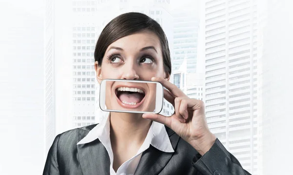 一个年轻女人用智能手机捂住嘴的画像 在银幕上笑着展示手机的女商人 具有城市景观背景的企业商人 移动通信布局 — 图库照片