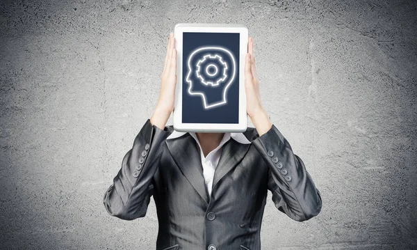 Portrait of woman covering her face with tablet computer. Businesswoman showing tablet PC with human head sign on screen. Corporate businessperson on grey wall background. Digital technology