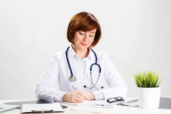 Belo médico sentado no escritório e escrevendo — Fotografia de Stock