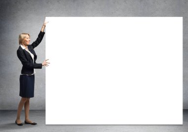 Takım elbiseli güzel bir kadın büyük beyaz pankartın yanında duruyor. İleti için kopyalama alanı olan boş bir beyaz tahta şablonu. İş kadını sunum ve tanıtım gibi bir şey. Ticari reklamcılık ve pazarlama.