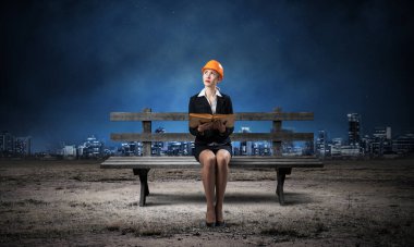 Dışarıdaki ahşap bankta oturan güzel bir mimar kadın. Turuncu kasklı genç bir teknisyen elinde açık bir kitap tutuyor. Mühendislik ve Geliştirme Şirketi