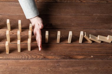 İş kadını, tahta domino taşlarını düşürerek domino etkisini engelliyor. Operatif iş çözümü, strateji ve başarılı müdahale. İş yardımı, koruma ve krizin önlenmesi