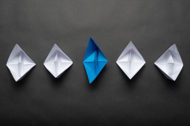 Siyah arka planda kağıt gemiler. Beyazlar arasında öncülük eden mavi kağıt gemiyle liderlik kavramı. Bireysel motivasyon ve yön. Kopya alanı olan sosyal pazarlama düzeni.