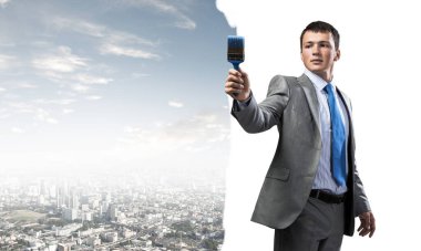 Elinde fırça tutan yaratıcı ressam gülümsüyor. Şehir planında takım elbiseli ve kravatlı neşeli yakışıklı bir adamın portresi. İş konseptinde hırs ve yaratıcılık