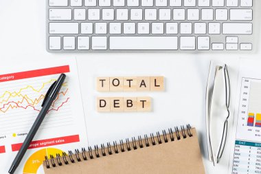 Küpler üzerindeki harflerle birlikte toplam borç kavramı. Malzemelerle dolu ofis hayatı. Düz beyaz yüzey, not defteri, bilgisayar klavyesi ve mali raporuyla yatıyordu. Sermaye yönetimi ve bankacılık.