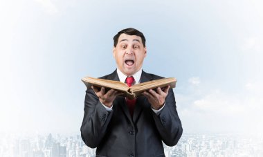 Ağzı açık kitap tutan sürpriz iş adamı. Bulutlu arka planda duran takım elbiseli ve kravatlı neşeli yetişkin adam. Eğitim ve bilgi. Profesyonel muhasebe