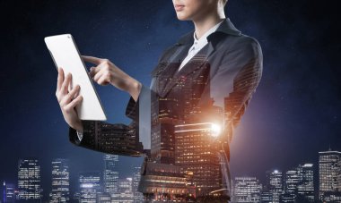 Tablet bilgisayar kullanan bir iş kadını. Gece kenti ve takım elbiseli kadınla çift pozlama konsepti. Emlak yatırımı. Emlak yönetimi ve geliştirme şirketinde dijital teknoloji.