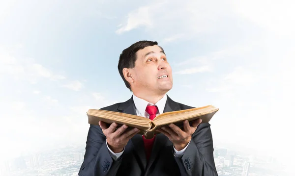 Serious businessman with open book looking up. Adult man in business suit standing on downtown background. Lawyer holding big legal regulation book. Professional business accounting and consulting