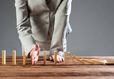 İş kadını, tahta domino taşlarını düşürerek domino etkisini engelliyor. Operatif iş çözümü, strateji ve başarılı müdahale. İş yardımı, koruma ve krizin önlenmesi