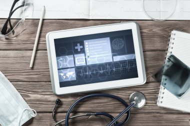 Beyaz tablet bilgisayar ve doktor aletleri ahşap masada.