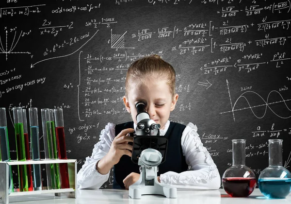 Маленькая девочка-ученый смотрит в микроскоп — стоковое фото