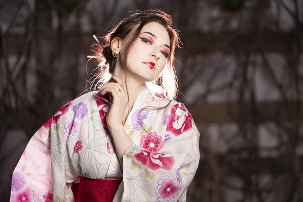 elegant girl in a classic traditional dress Japanese kimono white and pink standing alone on dark background in the studio