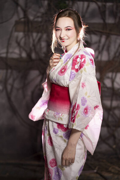 elegant girl in a classic traditional dress Japanese kimono white and pink standing alone on dark background in the studio