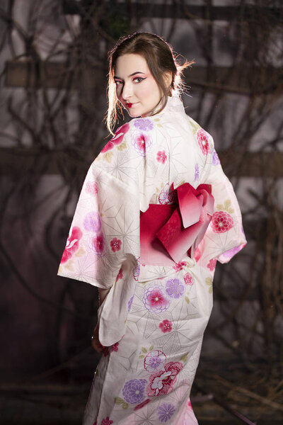 elegant girl in a classic traditional dress Japanese kimono white and pink standing alone on dark background in the studio