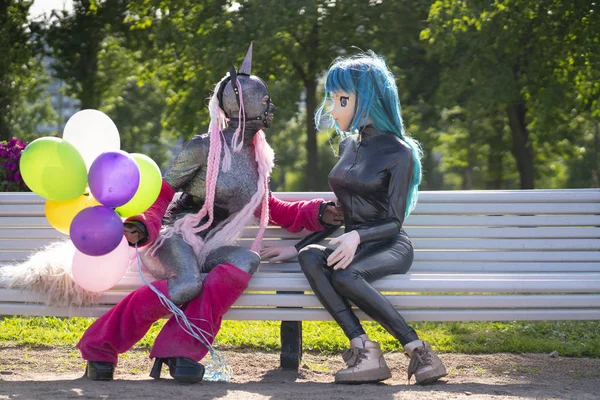 funny freaks, dressed in a unicorn bright costume and anime face mask with latex catsuit, enjoy life in the city Park