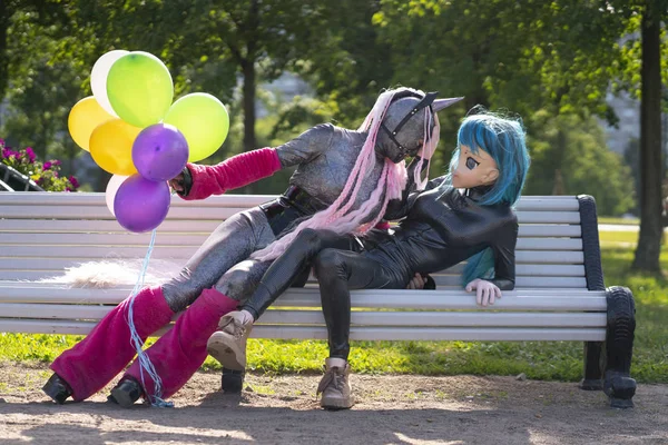 funny freaks, dressed in a unicorn bright costume and anime face mask with latex catsuit, enjoy life in the city Park