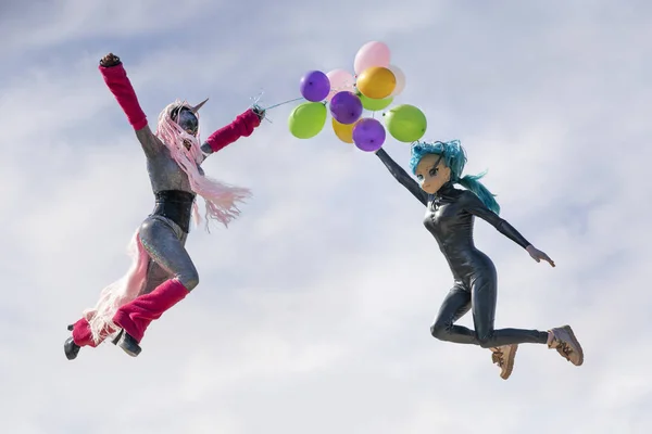 funny freaks, dressed in a unicorn bright costume and anime face mask with latex catsuit, enjoy life and jumping on the blue sky background