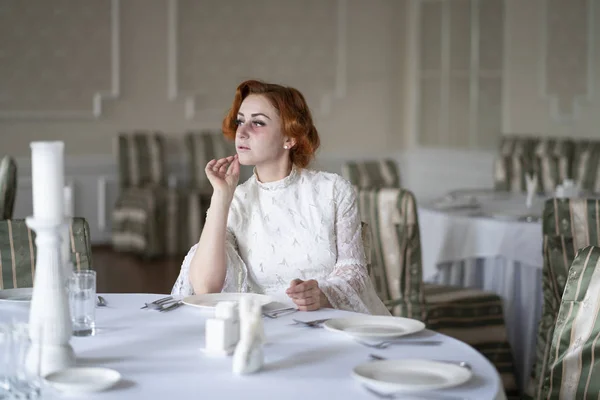 a dying seriously ill woman in a white dress waiting for Breakfast in an empty restaurant alone