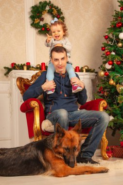 sevgi dolu bir baba ve tatlı kızı bir sandalyeye, ayakları büyük bir çoban köpeği oturmak, Noel için dekore edilmiş oda zevk