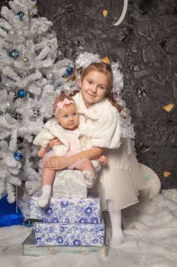 iki sevimli gerçek çocuk kız kardeşi siyah bir arka plan beyaz bir Noel ağacı ile birlikte poz