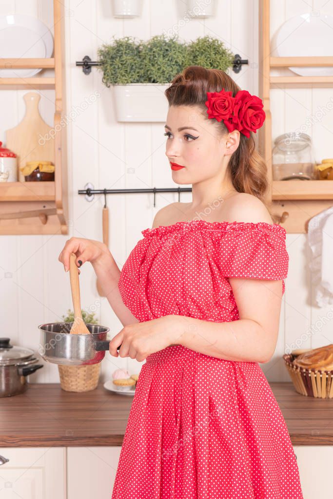 pretty plus size young woman wearing red pin up dress posing in her white kitchen at home alone