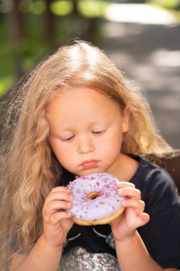 bir sandalyede oturuyor ve mor çörek yemek güzel sevimli küçük kız