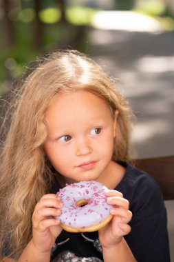 bir sandalyede oturuyor ve mor çörek yemek güzel sevimli küçük kız
