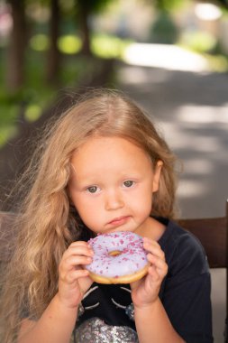 bir sandalyede oturuyor ve mor çörek yemek güzel sevimli küçük kız