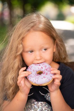 bir sandalyede oturuyor ve mor çörek yemek güzel sevimli küçük kız