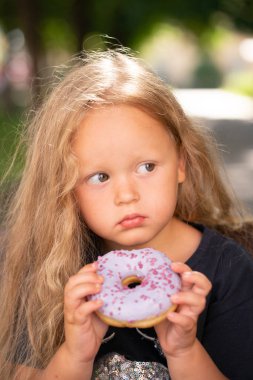 bir sandalyede oturuyor ve mor çörek yemek güzel sevimli küçük kız
