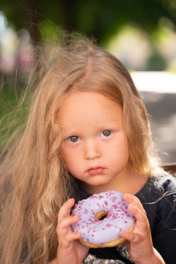 bir sandalyede oturuyor ve mor çörek yemek güzel sevimli küçük kız