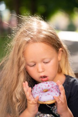 bir sandalyede oturuyor ve mor çörek yemek güzel sevimli küçük kız