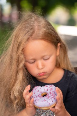 bir sandalyede oturuyor ve mor çörek yemek güzel sevimli küçük kız