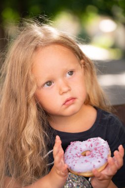 bir sandalyede oturuyor ve mor çörek yemek güzel sevimli küçük kız