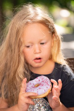 bir sandalyede oturuyor ve mor çörek yemek güzel sevimli küçük kız