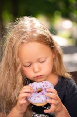 bir sandalyede oturuyor ve mor çörek yemek güzel sevimli küçük kız