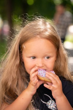 bir sandalyede oturuyor ve mor çörek yemek güzel sevimli küçük kız