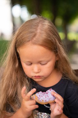 bir sandalyede oturuyor ve mor çörek yemek güzel sevimli küçük kız