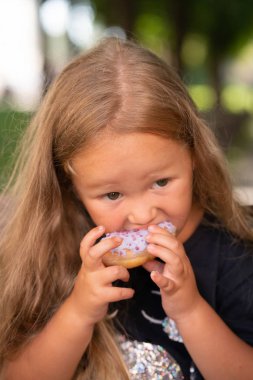bir sandalyede oturuyor ve mor çörek yemek güzel sevimli küçük kız