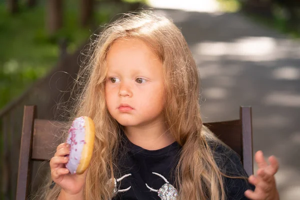 bir sandalyede oturuyor ve mor çörek yemek güzel sevimli küçük kız