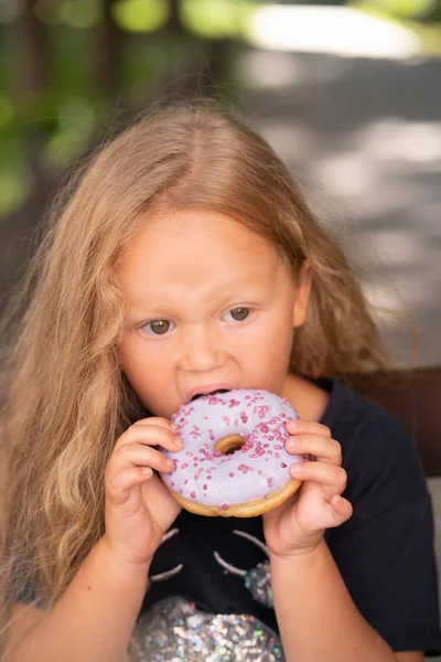 bir sandalyede oturuyor ve mor çörek yemek güzel sevimli küçük kız