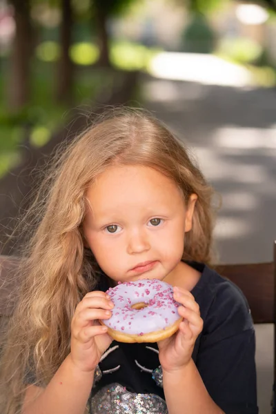 bir sandalyede oturuyor ve mor çörek yemek güzel sevimli küçük kız