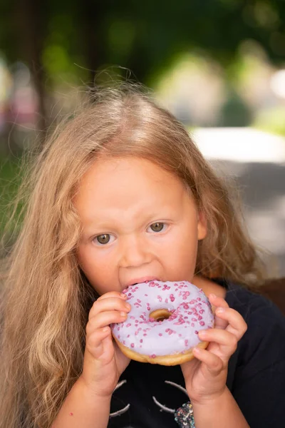 bir sandalyede oturuyor ve mor çörek yemek güzel sevimli küçük kız