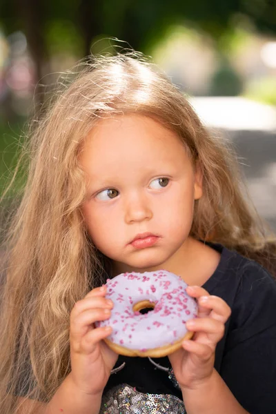 bir sandalyede oturuyor ve mor çörek yemek güzel sevimli küçük kız
